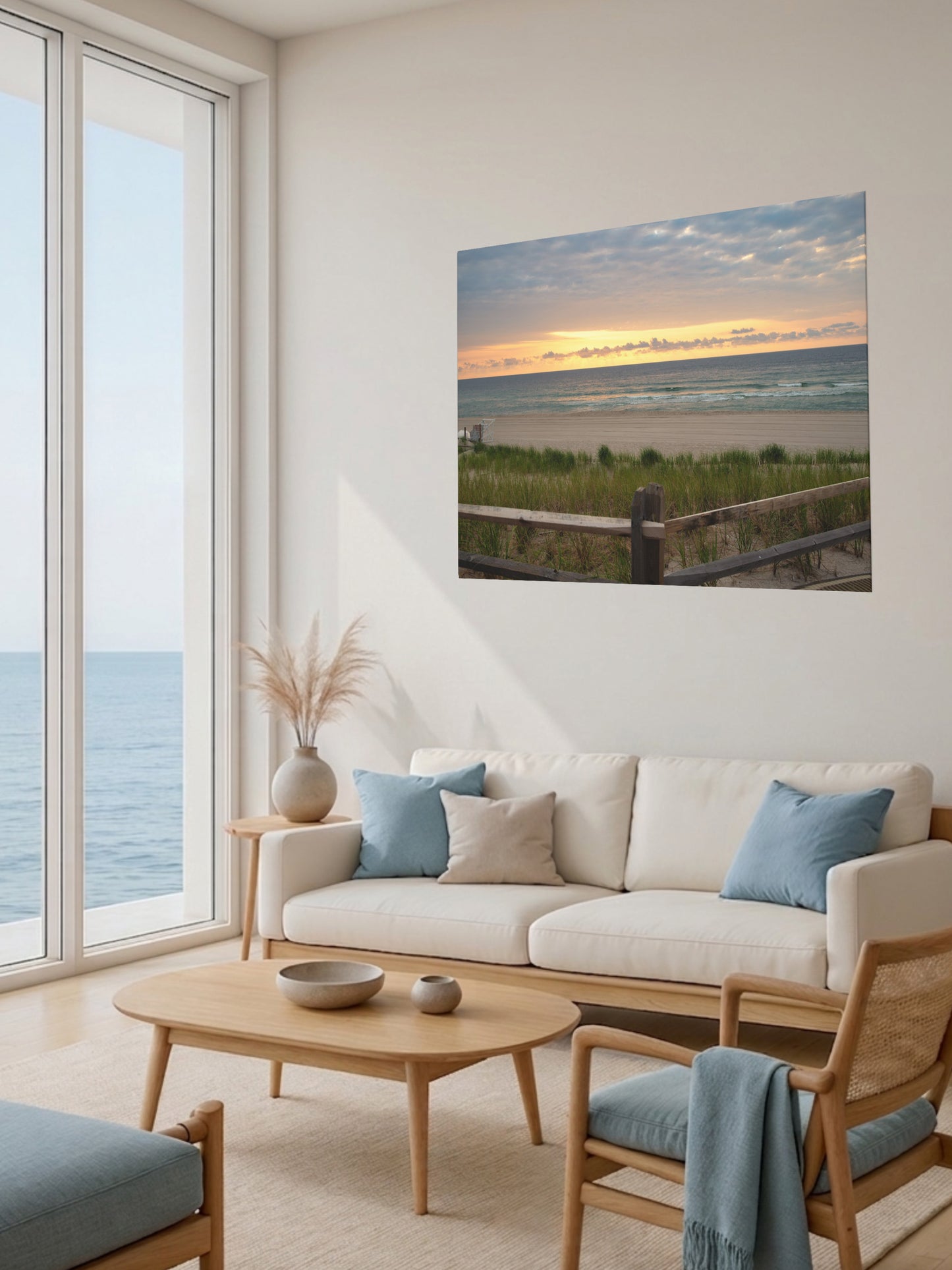 Living room with a large window view of the ocean, a beige sofa with blue cushions, and canvas print of a Jersey Shore sunrise over the Atlantic Ocean with beach dunes and grass.
