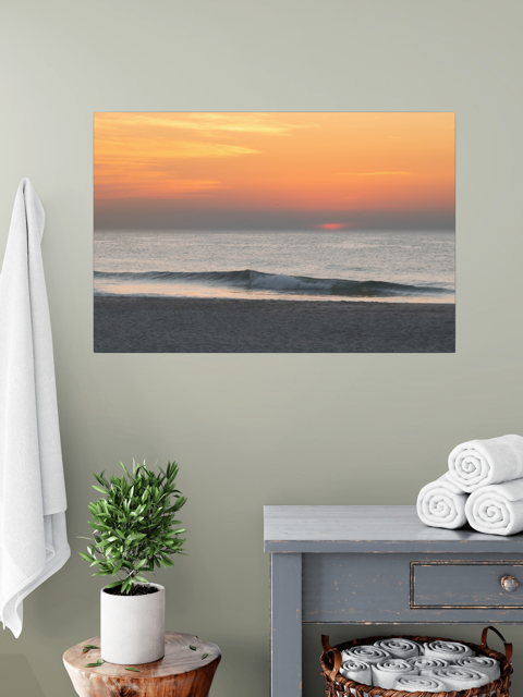 canvas print of a hazy sunrise over the ocean down the Jersey Shore hanging on a wall above a table with a plant and folded towels.