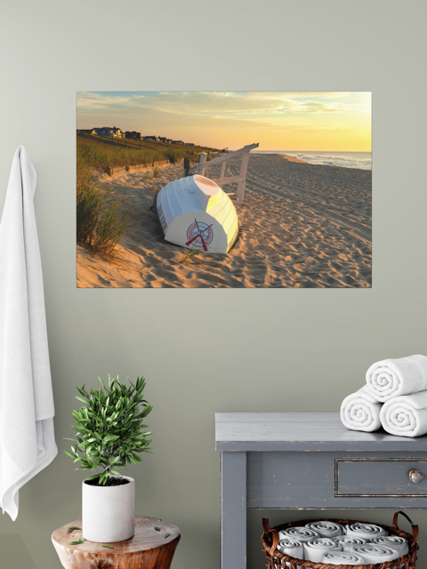 Canvas print of an overturned Jersey Shore Beach Patrol boat and lifeguard stand on the sand at sunrise with beach grass and rolling dunes over a grey table  with towels and plant.