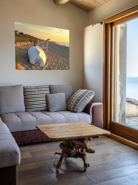 Living room with a gray sofa, wooden coffee table, and a canvas print of an overturned Jersey Shore Beach Patrol boat and lifeguard stand on the sand at sunrise with beach grass and rolling dunes