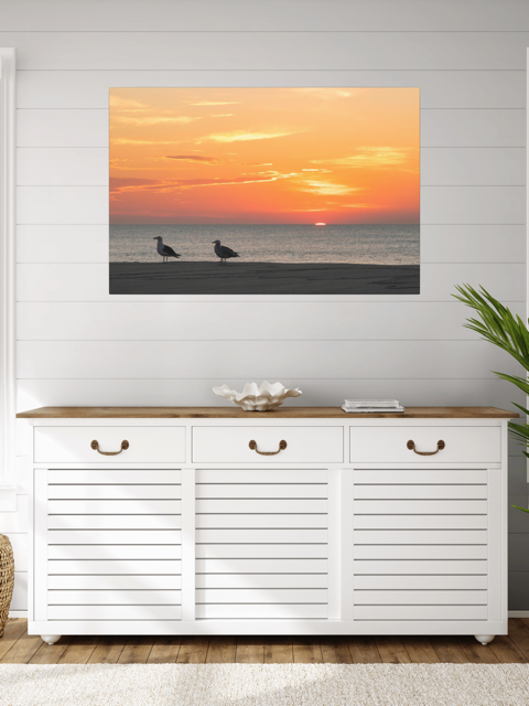 White cabinet with wooden top against a wall with a canvas print of two seagulls standing on a sandy Jersey Shore beach during a vibrant orange sunrise over the Atlantic Ocean.