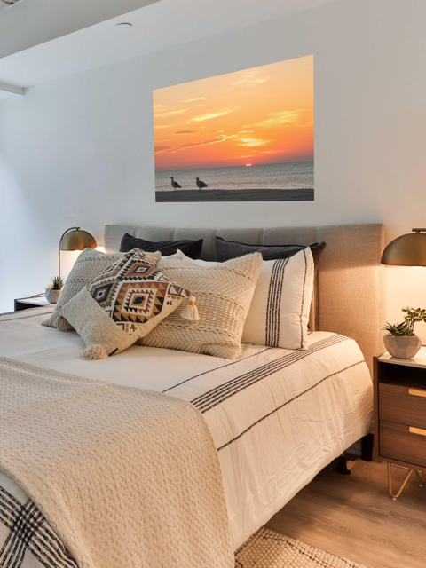 Bedroom with a canvas print of two seagulls standing on a sandy Jersey Shore beach during a vibrant orange sunrise over the Atlantic Oceanon the wall above the bed.
