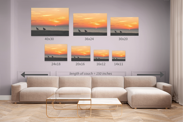 Living room with a beige sectional sofa and wall art displaying the same canvas print of two seagulls standing on a sandy Jersey Shore beach during a vibrant orange sunrise over the Atlantic Oceanin seven different sizes.