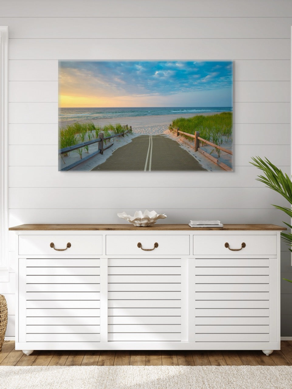 White cabinet with wooden top below a canvas print of a beach path on the Jersey Shore shortly after sunrise over the ocean on a white wall.