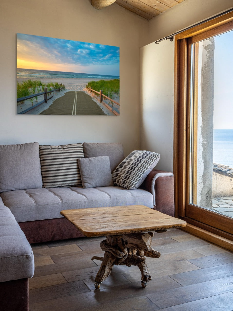Living room with a gray sofa, wooden coffee table, and a large canvas print of a beach path on the Jersey Shore shortly after sunrise over the ocean.
