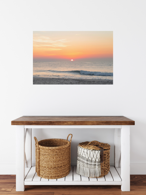 Wooden bench with two woven baskets underneath, featuring a canvas print featuring a summer sunrise over the Atlantic Ocean as seen from a quiet beach on the Jersey Shore on the wall.