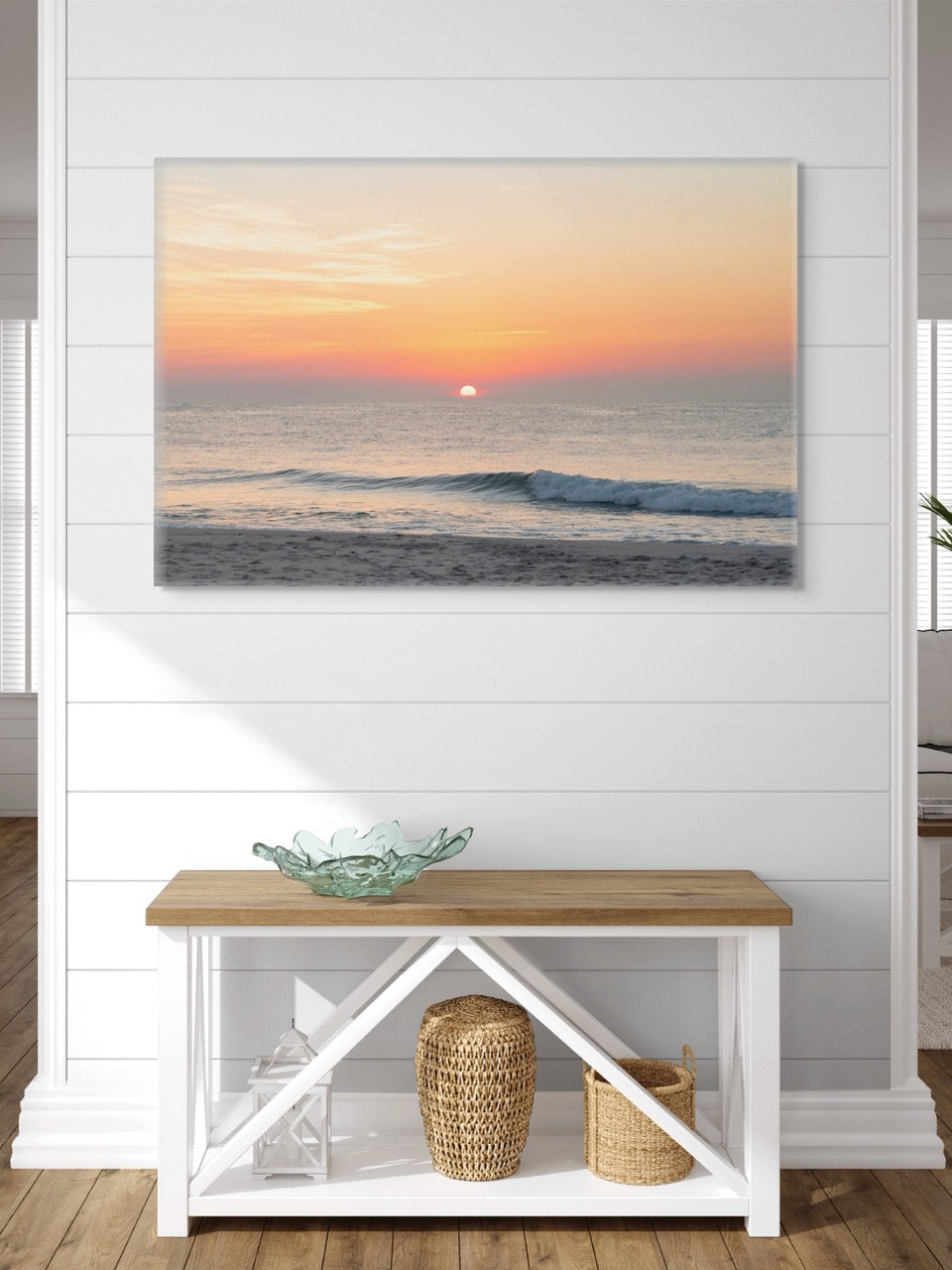 A canvas print featuring a summer sunrise over the Atlantic Ocean as seen from a quiet beach on the Jersey Shore on a wall above a wooden bench with decorative items.