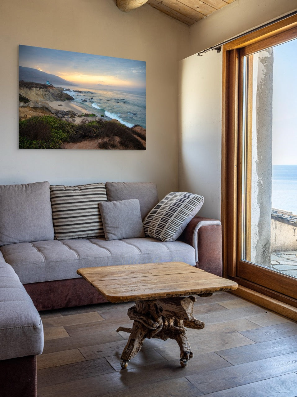 Living room with a gray sofa, wooden coffee table, and a large canvas print of the sunrise over the mountains as seen from the cliffs of Leo Carrillo State Beach near Malibu, California.