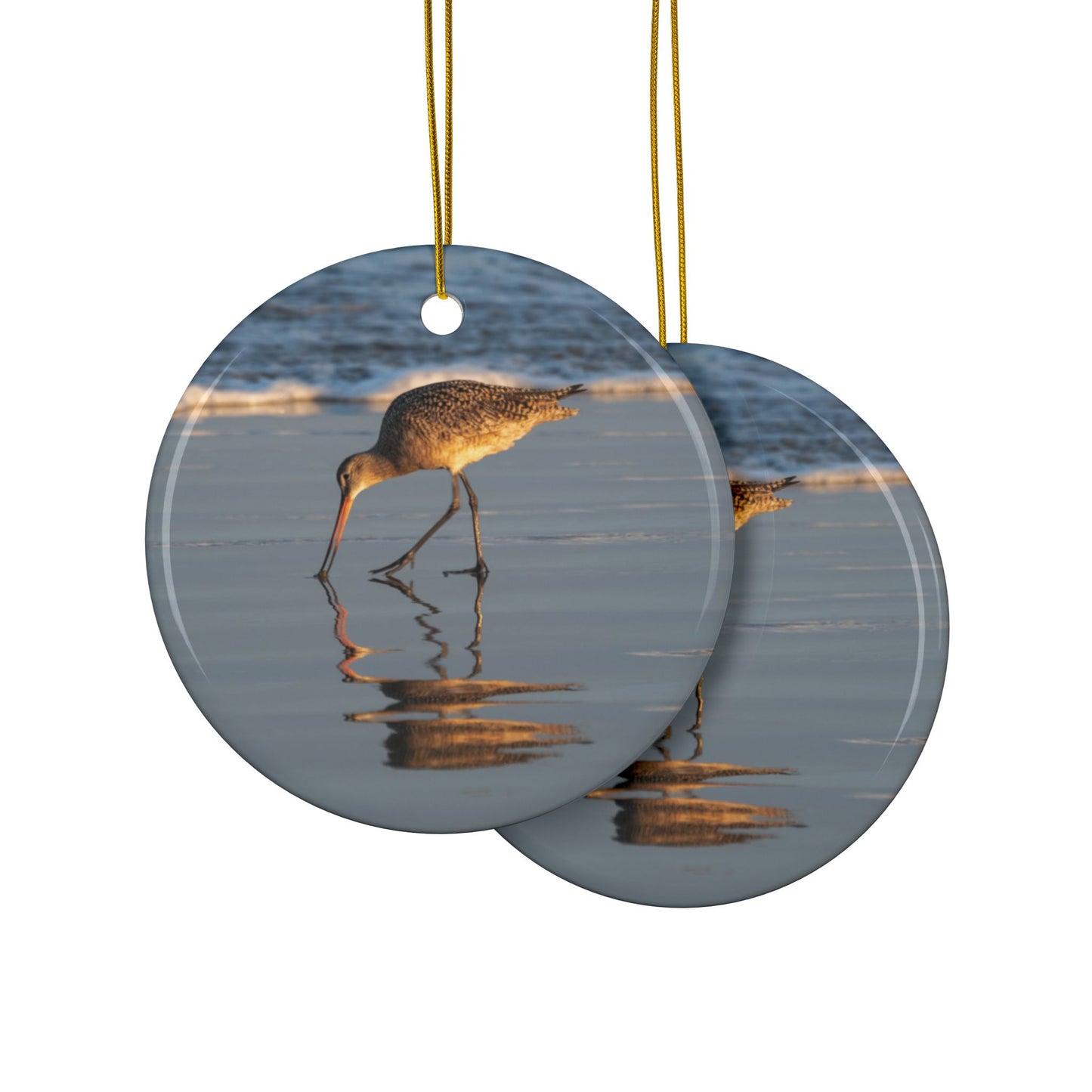 Front and back side of a ceramic holiday ornament featuring a photograph of a Long-billed Curlew mirrored in the wet sand of a shoreline under a soft golden sun