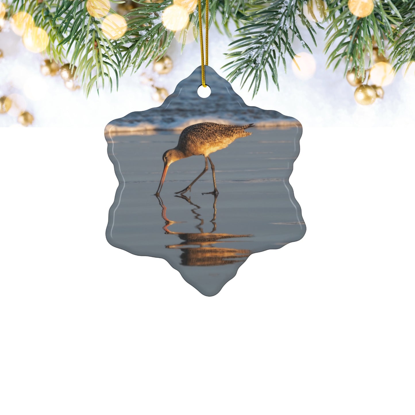 Ceramic holiday ornament featuring a photograph of a Long-billed Curlew mirrored in the wet sand of a shoreline under a soft golden sun on a white background