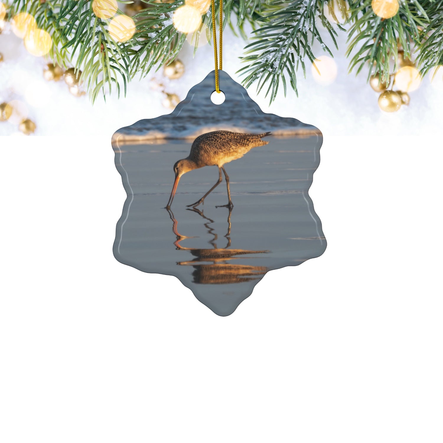 Ceramic holiday ornament featuring a photograph of a Long-billed Curlew mirrored in the wet sand of a shoreline under a soft golden sun on a white background