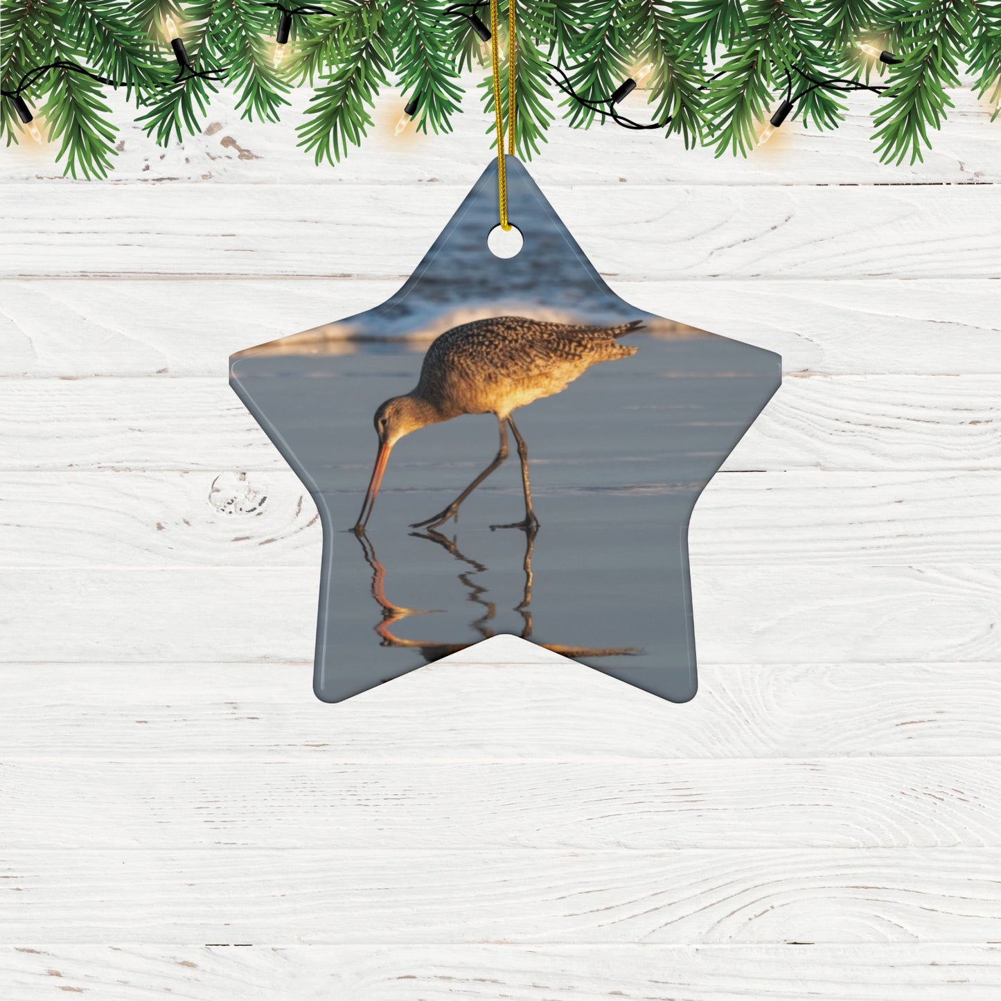 Star-shaped ceramic holiday ornament featuring a photograph of a Long-billed Curlew mirrored in the wet sand of a shoreline under a soft golden sun