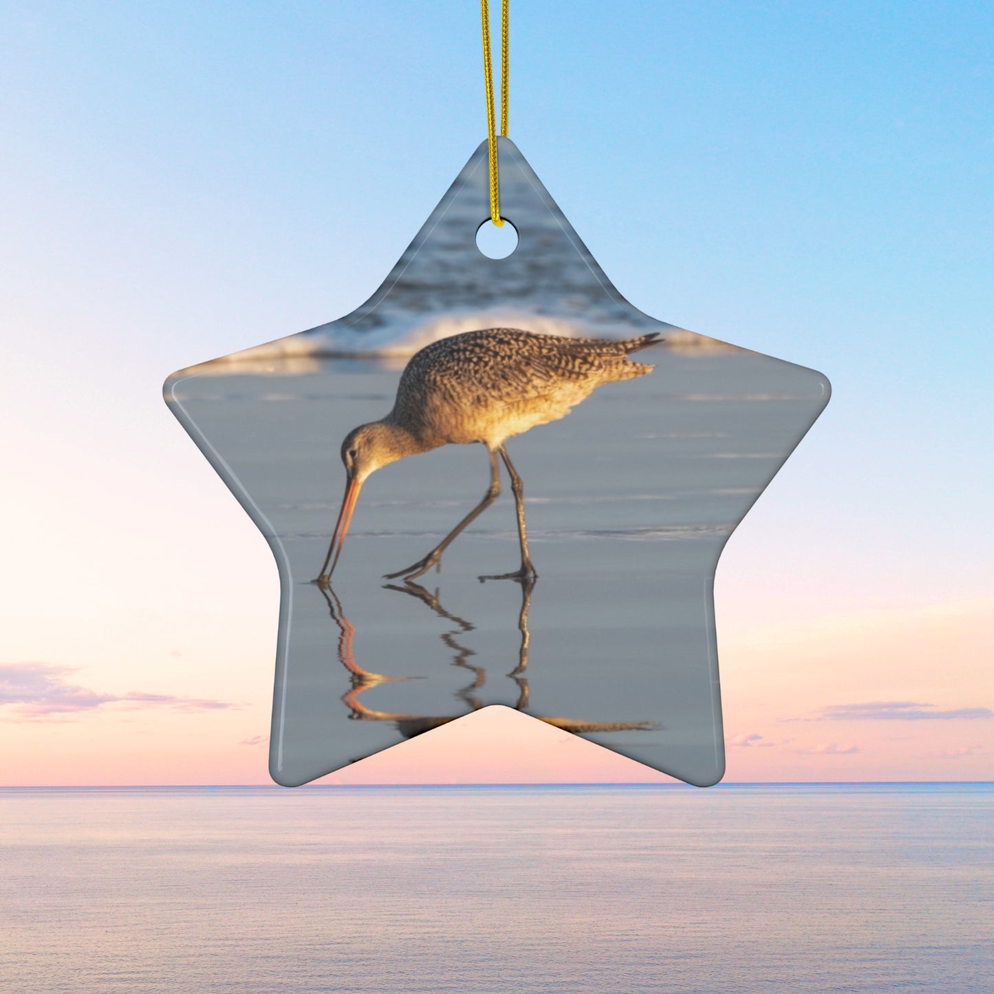 Star-shaped ceramic holiday ornament featuring a photograph of a Long-billed Curlew mirrored in the wet sand of a shoreline under a soft golden sun