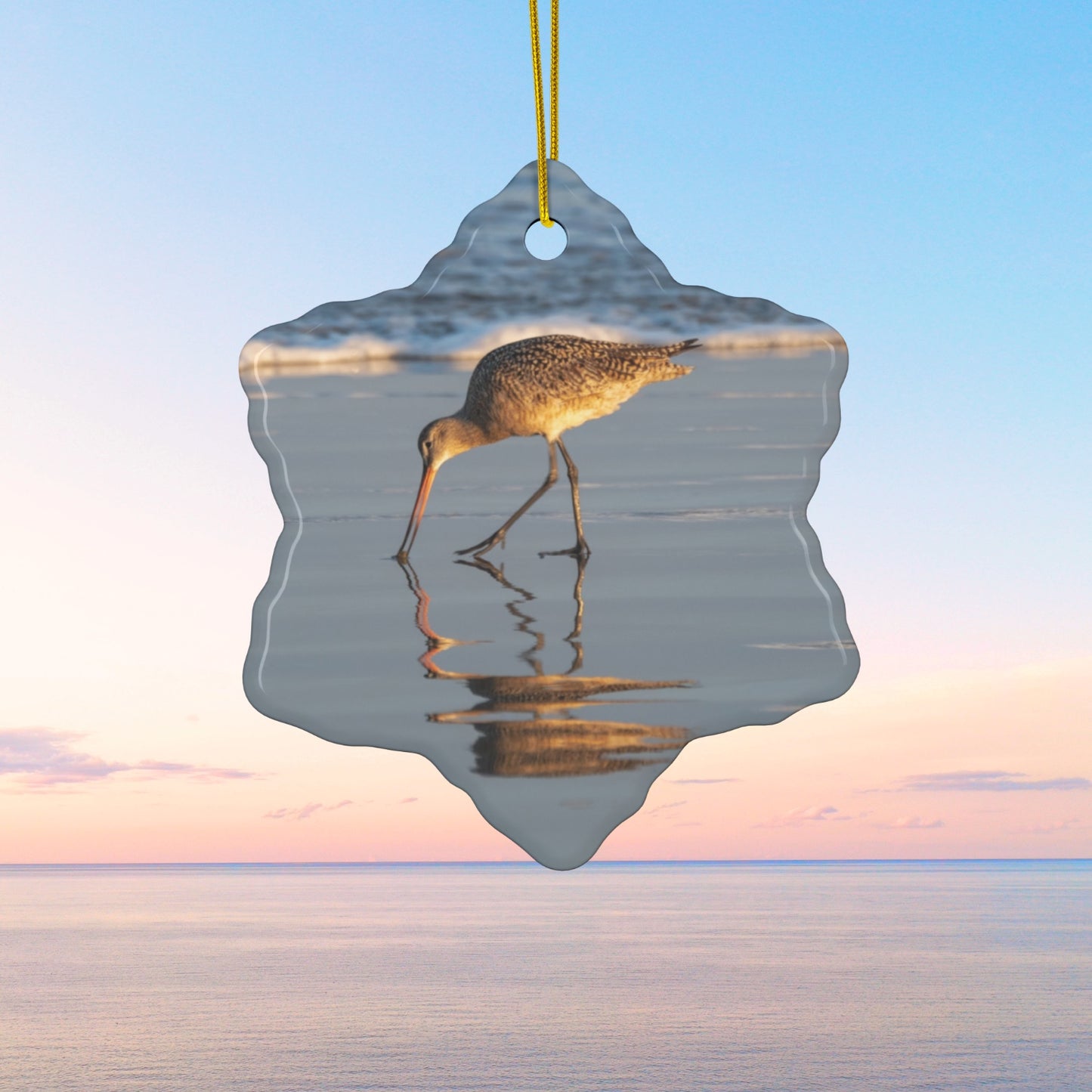 Ceramic holiday ornament featuring a photograph of a Long-billed Curlew mirrored in the wet sand of a shoreline under a soft golden sun