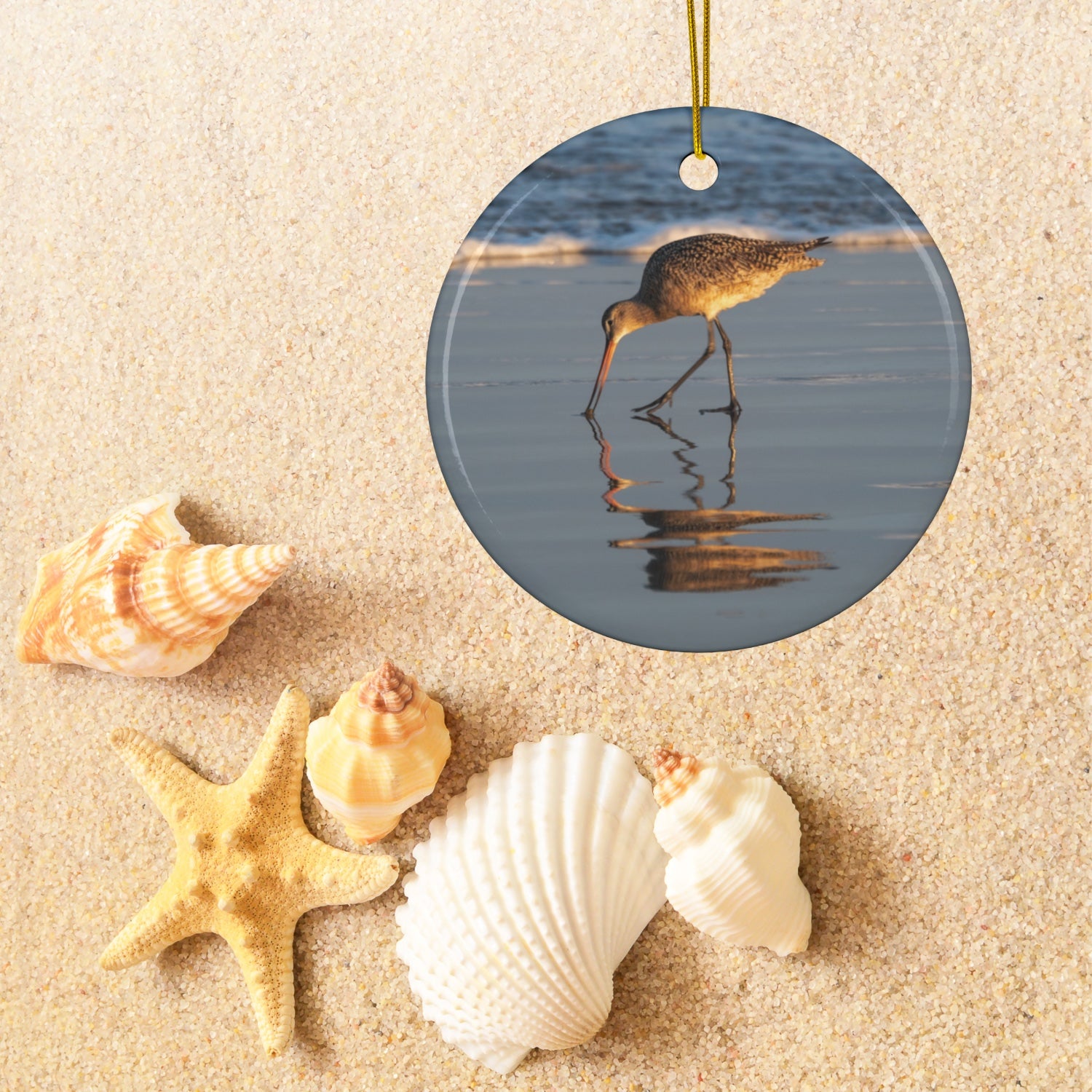 Ceramic holiday ornament featuring a photograph of a Long-billed Curlew mirrored in the wet sand of a shoreline under a soft golden sun