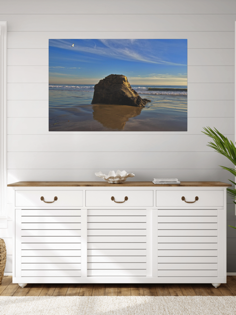 White storage cabinet with wooden top in a room with a canvas print of a rugged sea stack on a wet, reflective Malibu beach with a lone bird soaring in a clear blue sky over the Pacific Ocean on the wall.