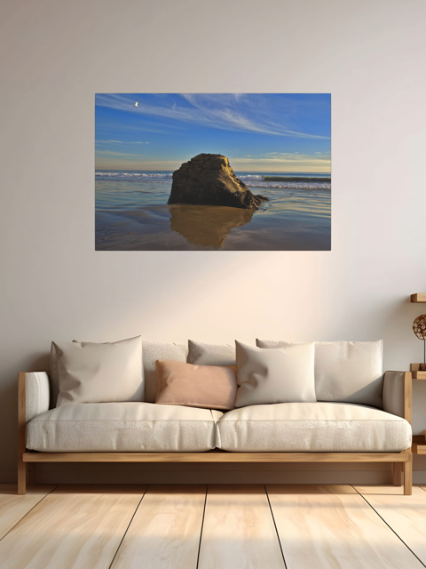 Canvas print of a rugged sea stack on a wet, reflective Malibu beach with a lone bird soaring in a clear blue sky over the Pacific Ocean above a white sofa with wooden frame