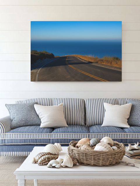 Sofa with decorative pillows and a coffee table with shells, featuring a canvas print of a winding mountain road above the Pacific Ocean in Malibu California.