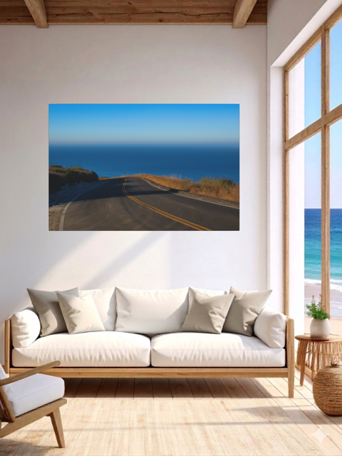 Living room with a canvas print of a winding mountain road above the Pacific Ocean in Malibu California, white sofa, and large windows.