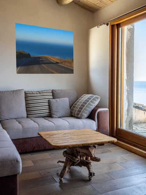 Living room with a gray sofa, wooden coffee table, and a canvas print of a winding mountain road above the Pacific Ocean in Malibu California.