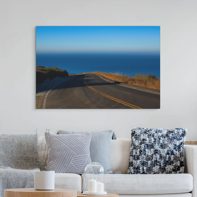 Sofa with decorative pillows and a canvas print of a winding mountain road above the Pacific Ocean in Malibu California.