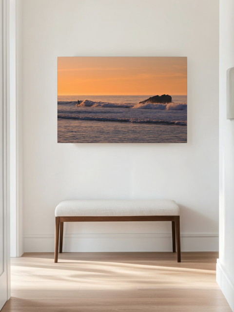 Canvas print featuring a surfer riding a wave at sunrise on a wall above a wooden bench in a room.