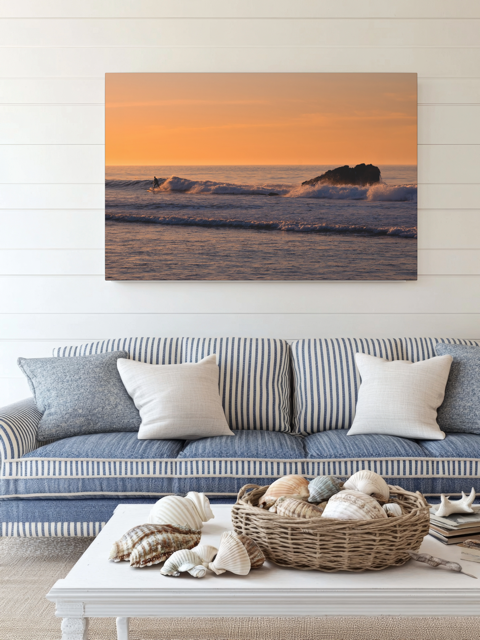 Living room with a couch, coffee table, and a canvas print featuring a surfer riding a wave at sunrise.