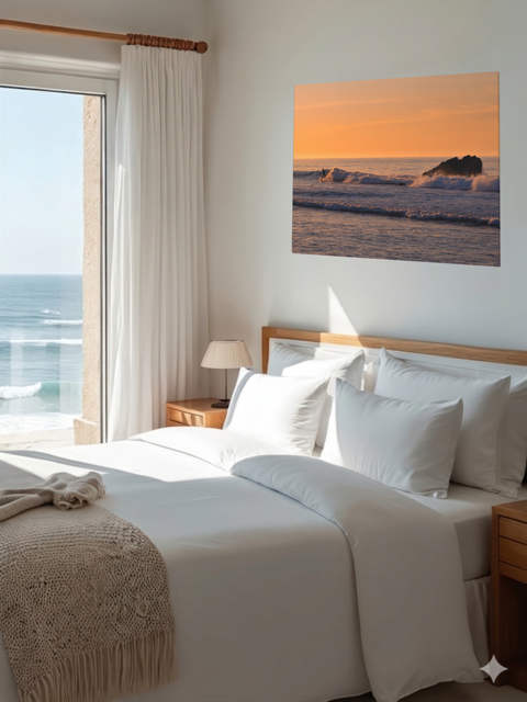Bedroom with a large bed, ocean view, and a canvas print featuring a surfer riding a wave at sunrise on the wall.