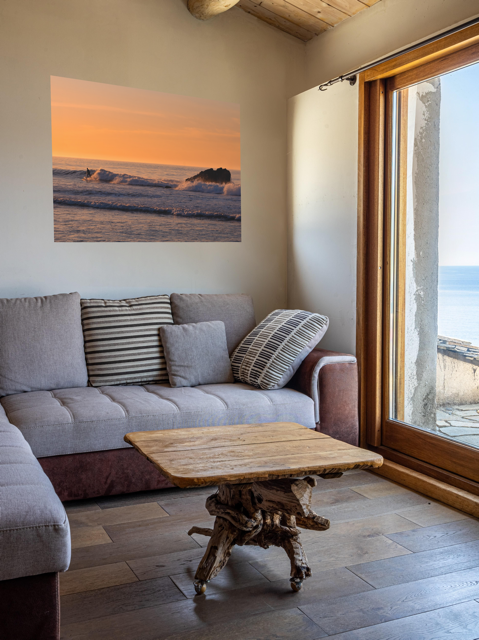 Living room with a gray sofa, wooden coffee table, and a lcanvas print featuring a surfer riding a wave at sunrise.