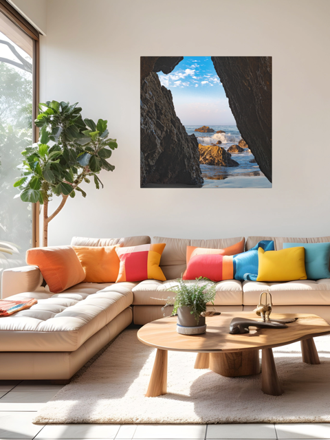 Modern living room with a sectional sofa, colorful pillows, and a canvas print of a view from inside a dark Malibu sea cave looking out at crashing ocean waves and rocks under a blue sky on the wall.