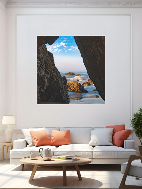 Living room with a canvas print of a view from inside a dark Malibu sea cave looking out at crashing ocean waves and rocks under a blue sky.