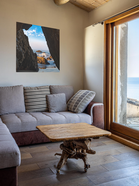 Living room with a gray sofa, wooden coffee table, and a canvas print of a view from inside a dark Malibu sea cave looking out at crashing ocean waves and rocks under a blue sky.