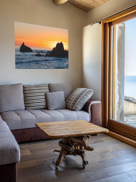 Living room with a gray sofa, wooden coffee table, and a canvas print of an ocean sunset with rocks.