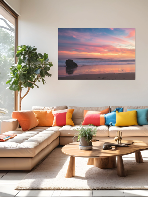 Modern living room with a sectional sofa, colorful pillows, and a canvas print of a solitary rock sea stack on a Malibu beach at sunset with a vibrant pink, orange, and purple sky reflected in the wet sand.