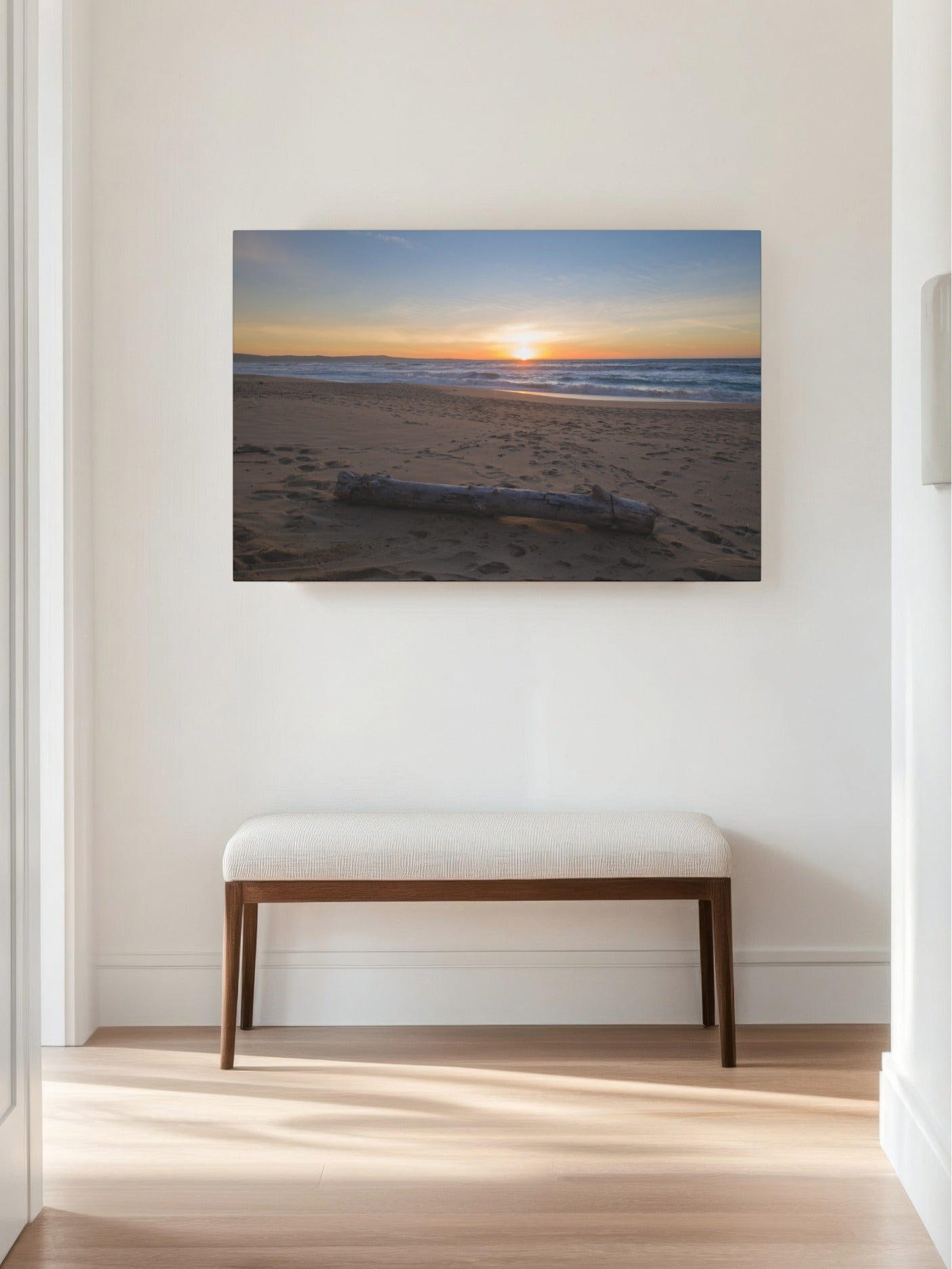 Canvas print of a Monterey California beach sunset with large driftwood log on sand on a wall above a bench in a room with wooden floor.