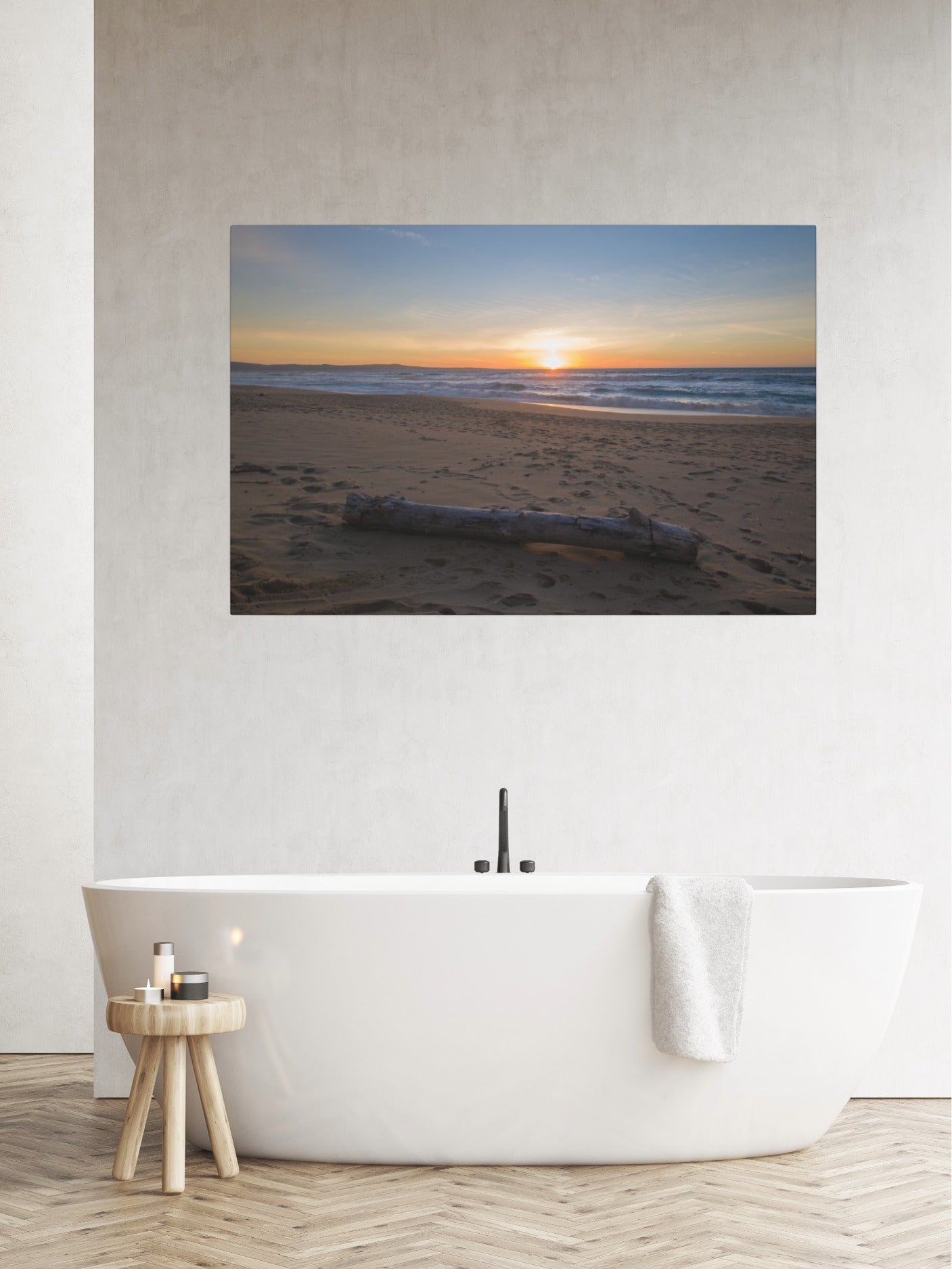 Canvas print of a Monterey California beach sunset with large driftwood log on sand on a wall above a modern white bathtub in a bathroom.