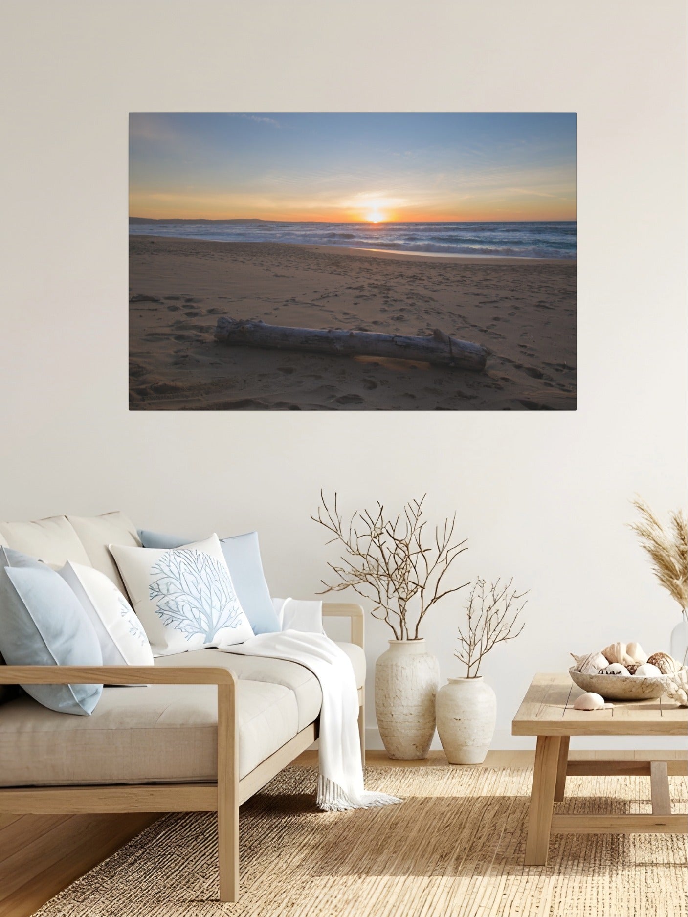 Canvas print of a Monterey California beach sunset with large driftwood log on sand on a wall above a living room sofa with decor items.