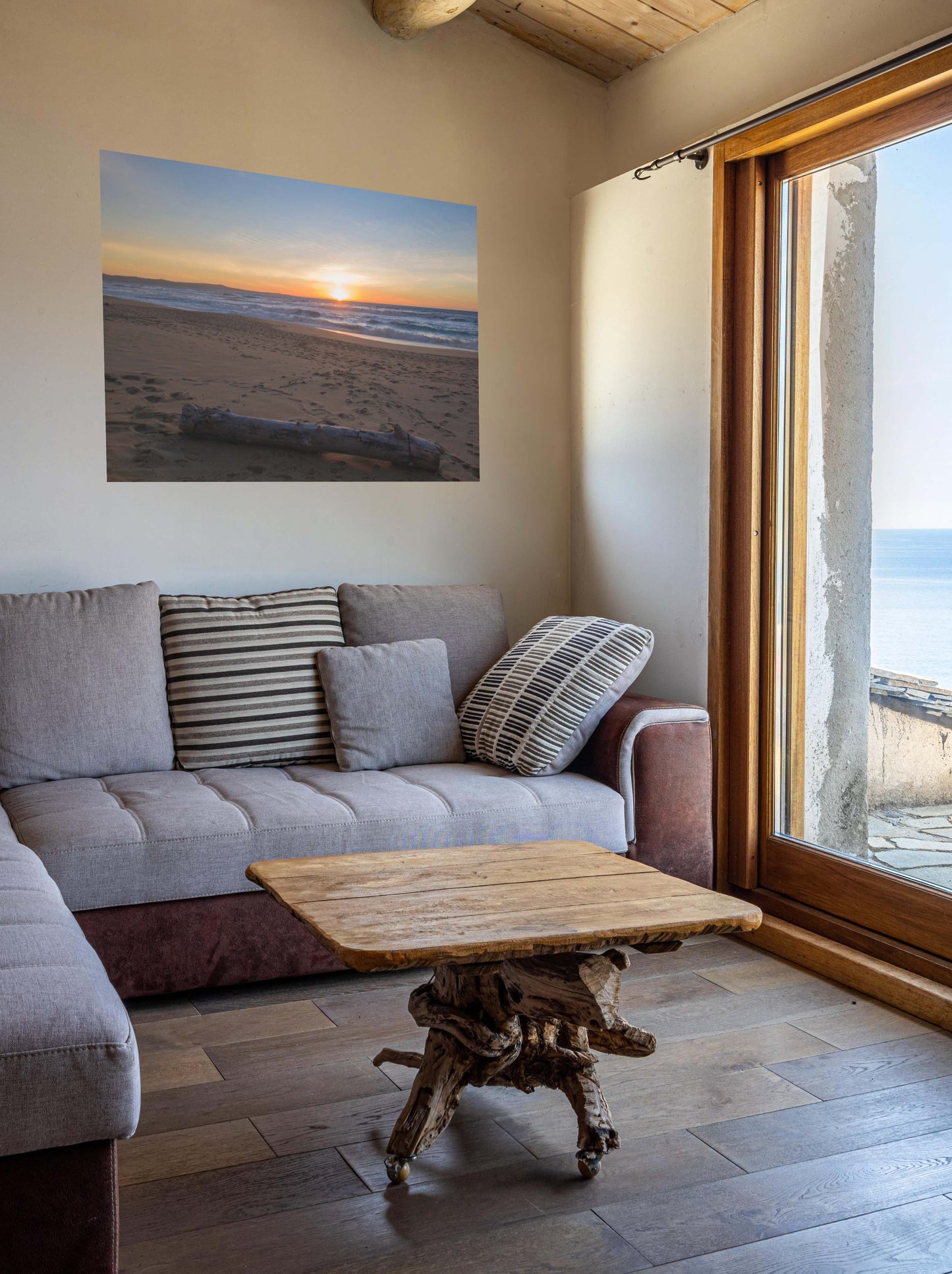 Living room with a gray sofa, wooden coffee table, and a canvas print of a Monterey California beach sunset with large driftwood log on sand