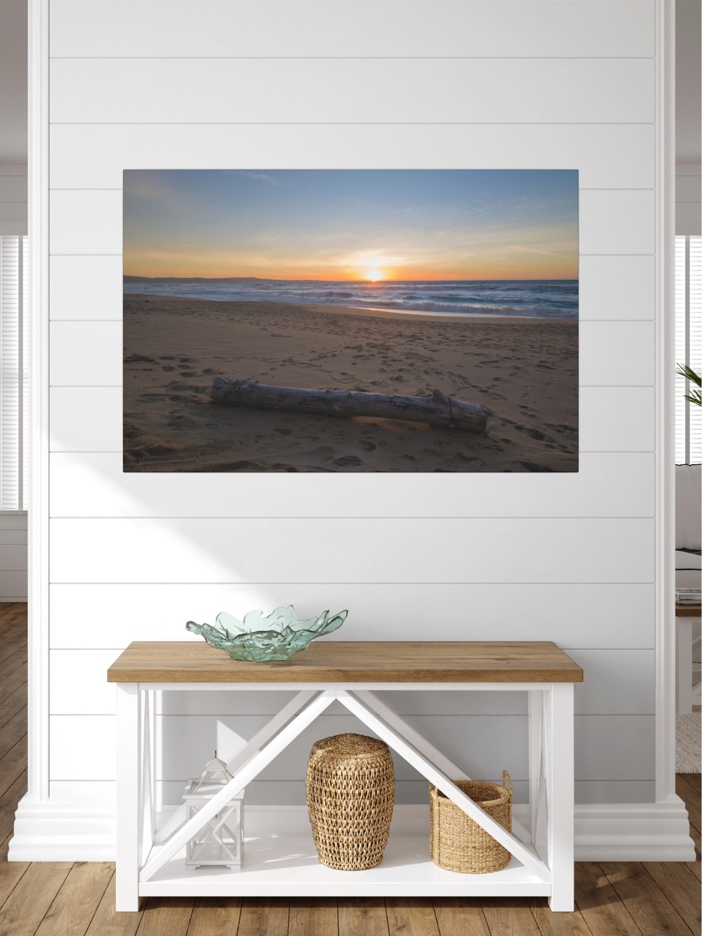 Canvas print of a Monterey California beach sunset with large driftwood log on sand on a wall above a wooden console table with decorative items.