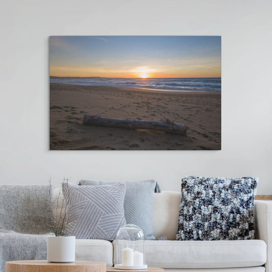 Canvas print of a Monterey California beach sunset with large driftwood log on sand on a wall above a sofa with decorative pillows.