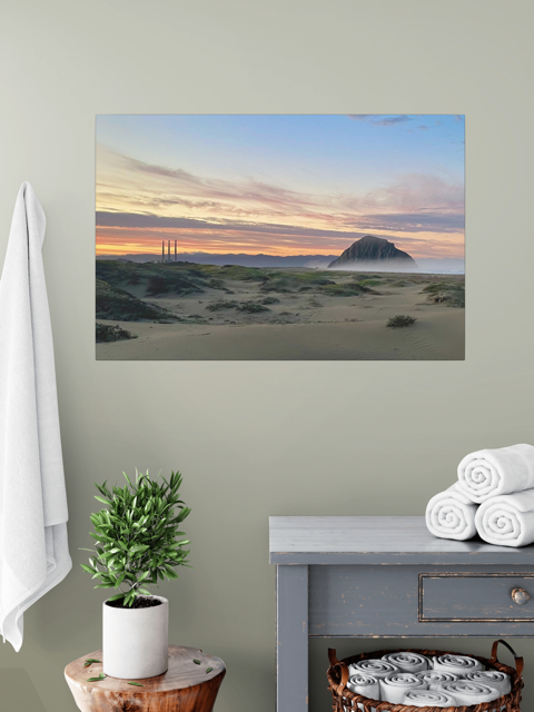 Vibrant sunrise over Morro Rock and Three Stacks from beach dunes canvas print in a room with a plant and towels.