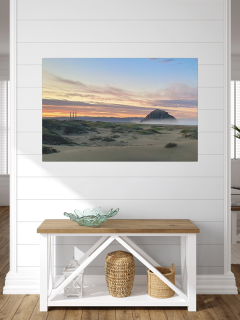 Vibrant sunrise over Morro Rock and Three Stacks from beach dunes canvas print on a white wall above a wooden bench with storage baskets.