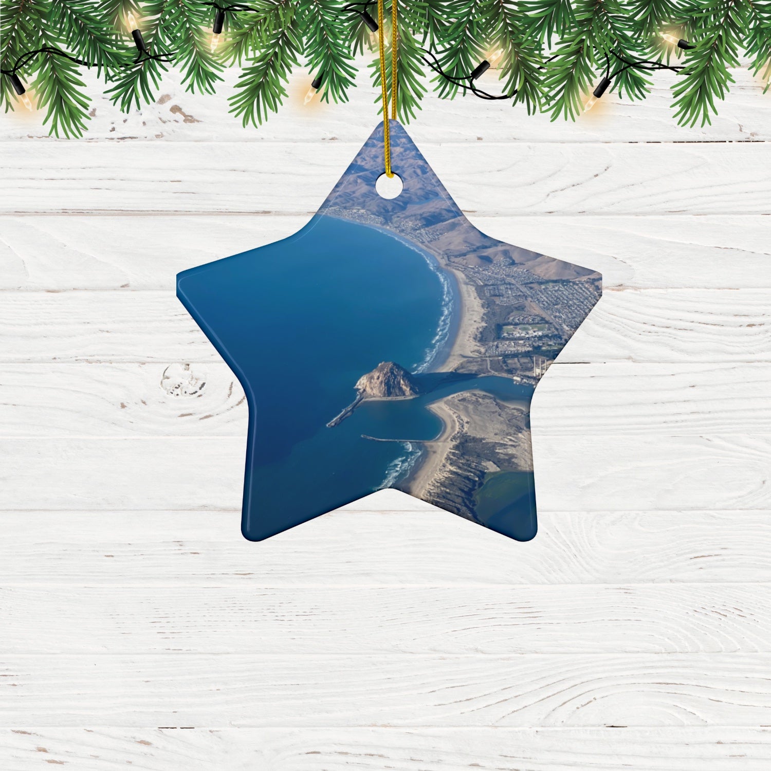 Star-shaped Ceramic holiday ornament featuring an aerial photograph of Morro Rock and the coastline of Morro Bay, California, with vibrant blue water and golden hills on a white wooden background