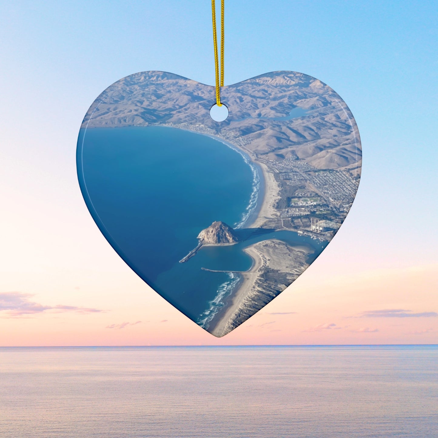 Heart shaped ceramic holiday ornament featuring an aerial photograph of Morro Rock and the coastline of Morro Bay, California, with vibrant blue water and golden hills