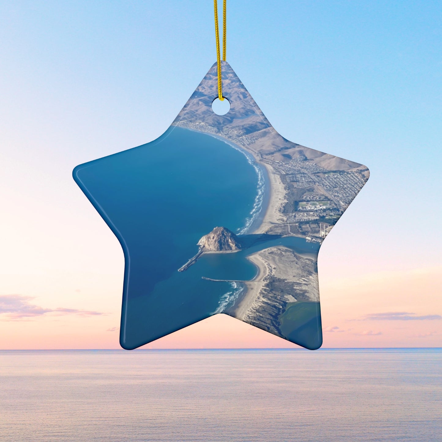 Star-shaped ceramic holiday ornament featuring an aerial photograph of Morro Rock and the coastline of Morro Bay, California, with vibrant blue water and golden hills