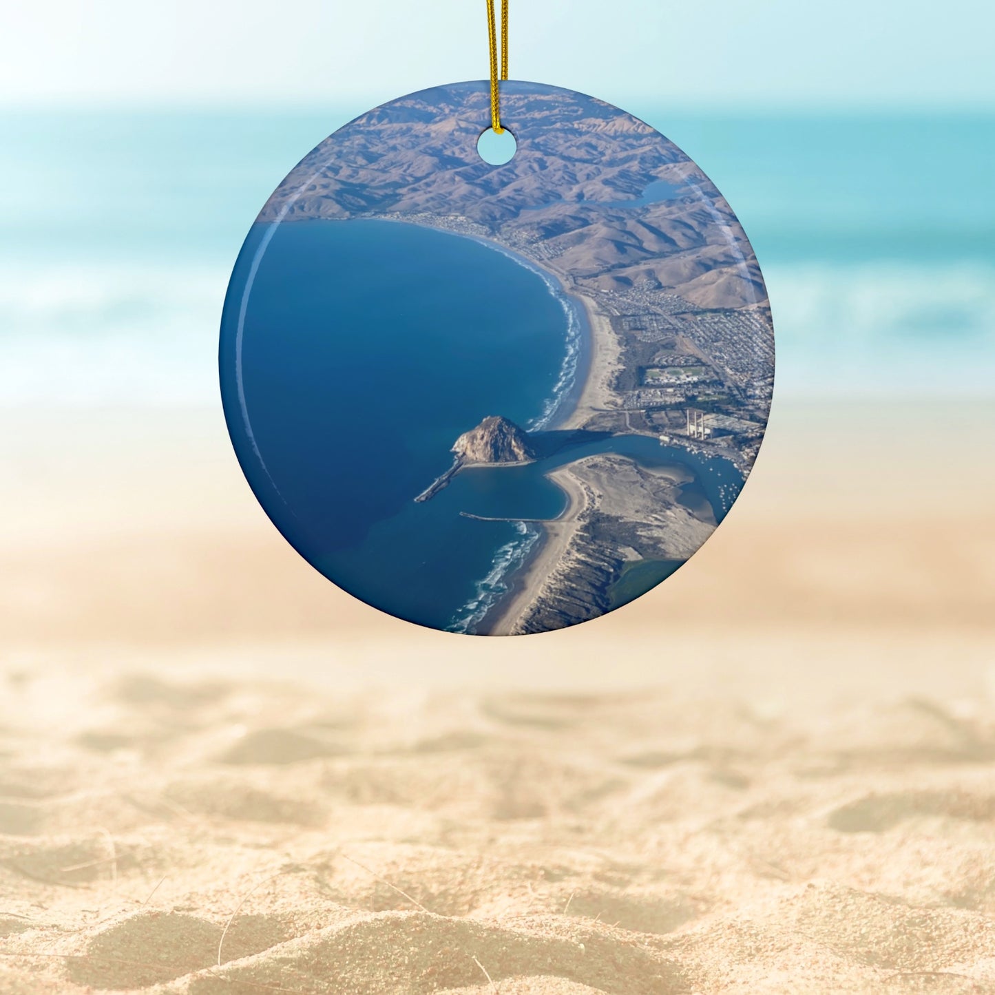 Ceramic holiday ornament featuring an aerial photograph of Morro Rock and the coastline of Morro Bay, California, with vibrant blue water and golden hills