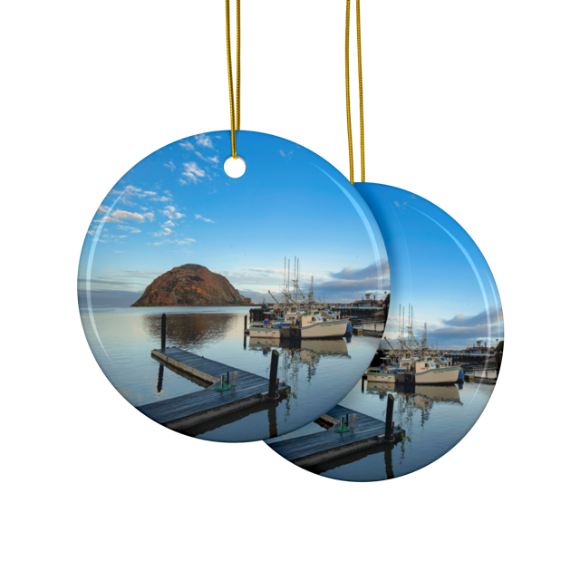 Front and back side of a ceramic Christmas ornament featuring an early morning photograph of Morro Bay harbor with boats, a pier, and Morro Rock reflected in the calm water