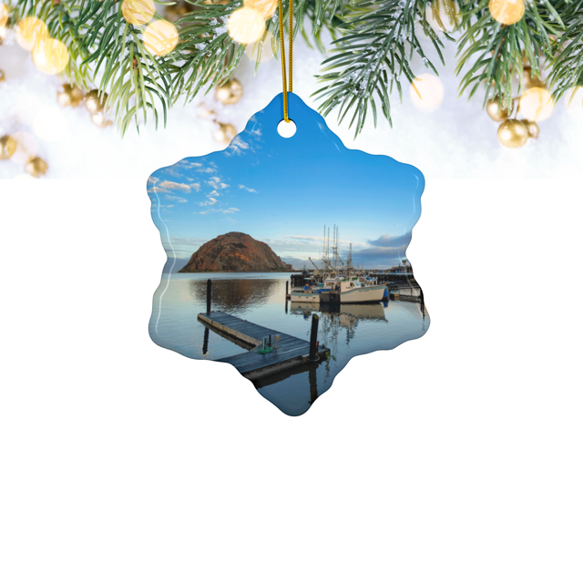 Ceramic Christmas ornament featuring an early morning photograph of Morro Bay harbor with boats, a pier, and Morro Rock reflected in the calm water, surrounded by Christmas lights and greenery.