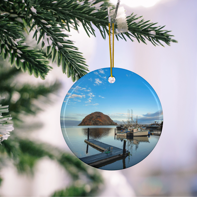 Ceramic Christmas ornament featuring an early morning photograph of Morro Bay harbor with boats, a pier, and Morro Rock reflected in the calm water, hanging on a Christmas tree.
