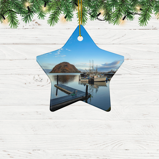 Star-shaped ceramic Christmas ornament featuring an early morning photograph of Morro Bay harbor with boats, a pier, and Morro Rock reflected in the calm water, hanging against a white wooden background.